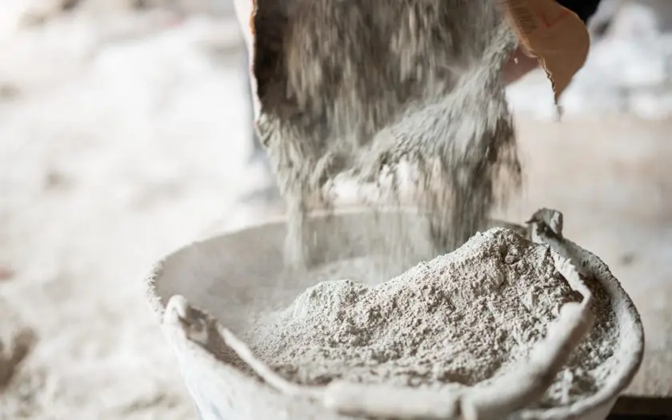 Close-up of a worker filling a bucket with cement from a bag at construction site