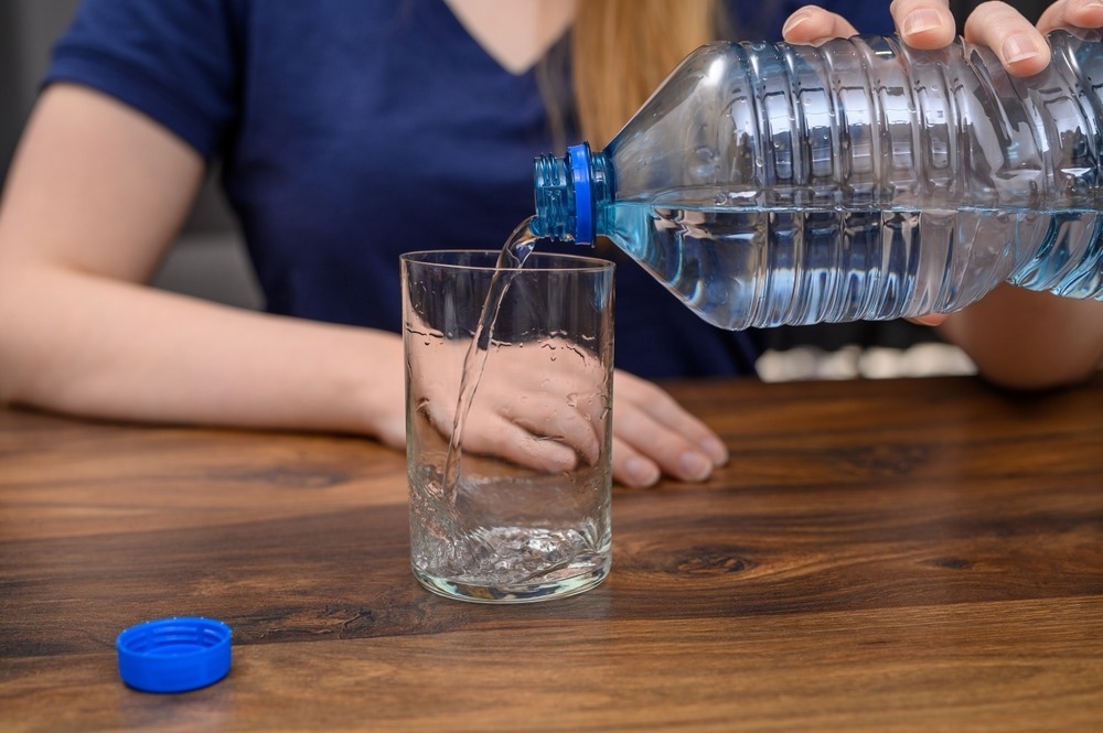 water bottle, microplastics, woman pouring water into glass