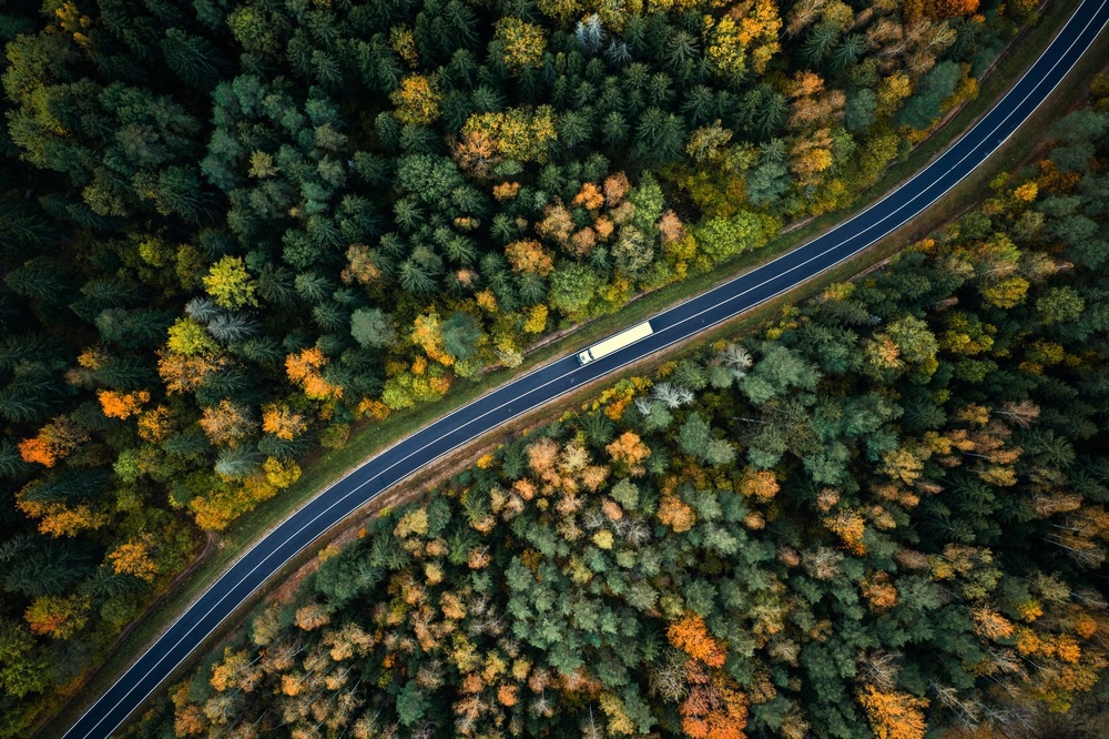 Arial view of heavy truck on a narrow twisting road. Autumn colorful trees by the sides of the road.
